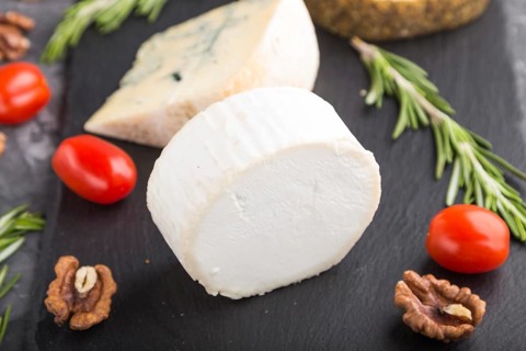 White goat cheese and various types of cheese with rosemary and tomatoes on black slate board on a