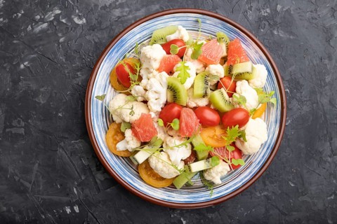 Vegetarian salad of cauliflower cabbage, kiwi, tomatoes, microgreen sprouts on black concrete