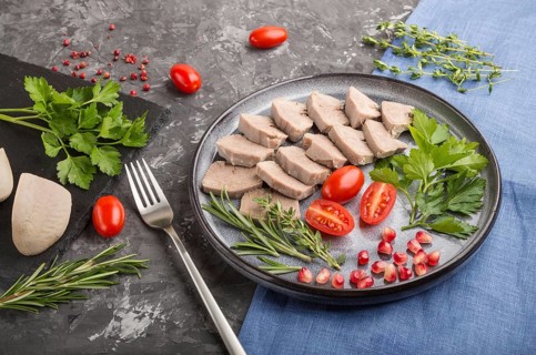 Boiled pork tongue with tomatoes and herbs on a black concrete background and blue linen textile.