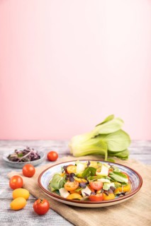 Vegetarian salad of pac choi cabbage, kiwi, tomatoes, kumquat, microgreen sprouts on gray and pink