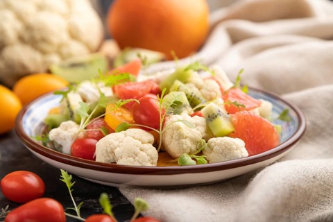 Vegetarian salad of cauliflower cabbage, kiwi, tomatoes, microgreen sprouts on black concrete