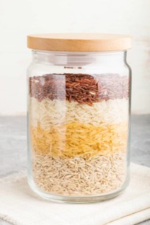 Glass jar with different kinds of rice poured in layers on a gray and white background. side view,