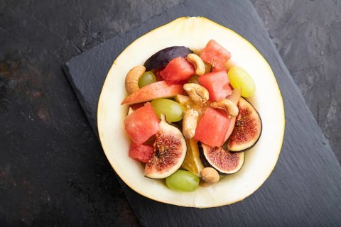 Vegetarian fruit salad of watermelon, grapes, figs, pear, orange, cashew on slate board on a black