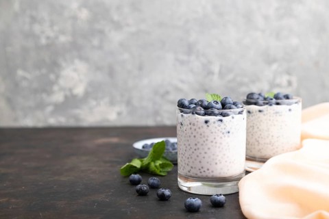 Yogurt with blueberry and chia in glass on black concrete background and orange linen textile. Side