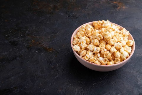 Popcorn with caramel in ceramic bowl on a black concrete background. Side view, copy space