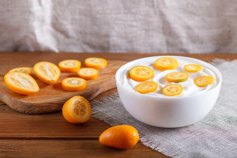 Greek yogurt with kumquat pieces in a white plate on a brown wooden background, close up