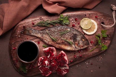 Fried dorado fish, with spices and herbs, on a wooden board, pomegranate sauce, close-up, no people