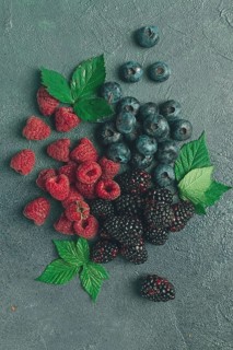 A mix of ripe berries, with leaves scattered on the table, raspberries, blackberries, blueberries,