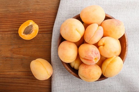Fresh orange apricots in wooden bowl on wooden background. top view, flat lay, close up