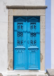 Blue old door with decorative ironwork in a stone frame in front of a white Mediterranean-style
