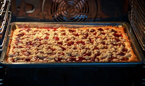 A plum tart with red plums and crumb topping is baking in the oven, ready for perfection