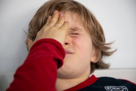 Kind mit Kopfschmerzen, Junge 9 Jahre alt, mit schmerzverzerrtem Gesicht, symbolisches Bild