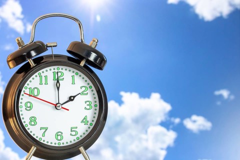 Symbolic image of the time change to summer time: close-up of an alarm clock in front of a blue sky