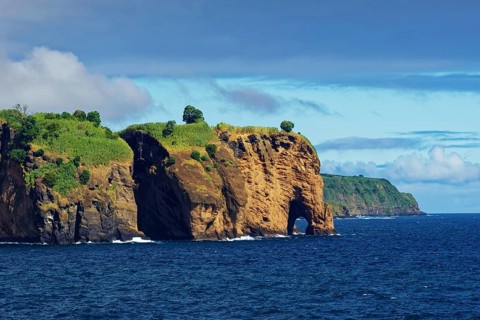 Rocks looking like a giant elephant covered with green trees and blue water under a clear sky,