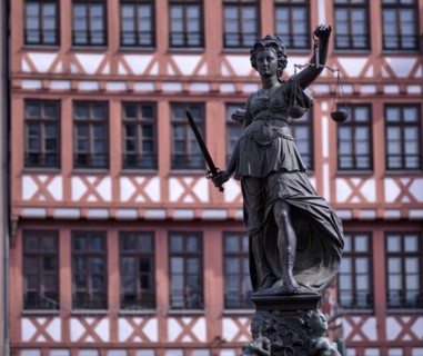 Justitia, Roman goddess of justice, with scales but without blindfold, in front of half-timbered
