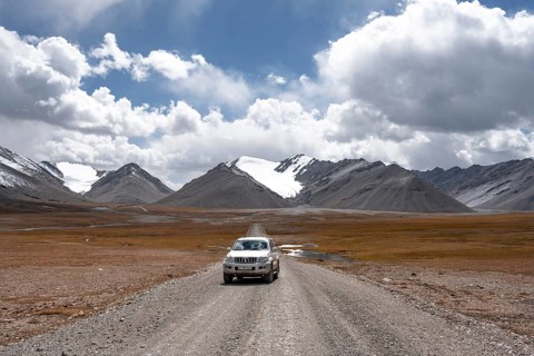 Off-road vehicle on a gravel track, glaciated and snow-covered peaks, Ak Shyrak Mountains, near