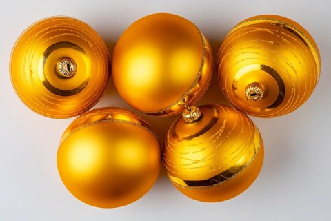 Five golden Christmas baubles lie on a white surface