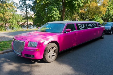 An eye-catching pink limousine parked on the roadside under trees in daylight, stretch limousine,