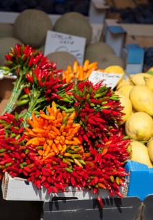 Different coloured peppers on a market stall next to other fruits