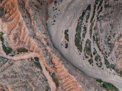 Off-road vehicle on a track in a riverbed, landscape of eroded hills, top-down, badlands, aerial