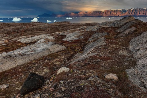 Evening light and atmosphere in fjord with icebergs in front of steep mountains, cloudy, autumn,