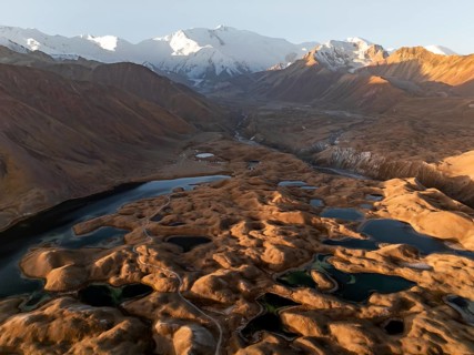 White glaciated and snowy mountain peak Pik Lenin at sunrise, hilly landscape with golden yellow