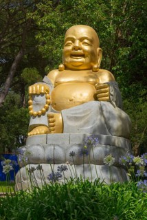 Golden Buddha statue, surrounded by flowers and green nature, radiates peace and spirituality under