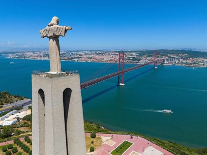 Statue with outstretched arms on a viewpoint next to a red bridge and an extensive cityscape in the