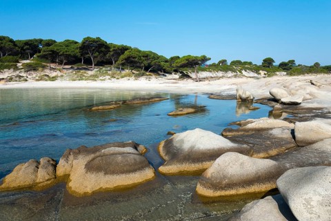 Tranquil coastal view with rocks and a sandy shore under a clear sky, Karidi beach, Karydi,
