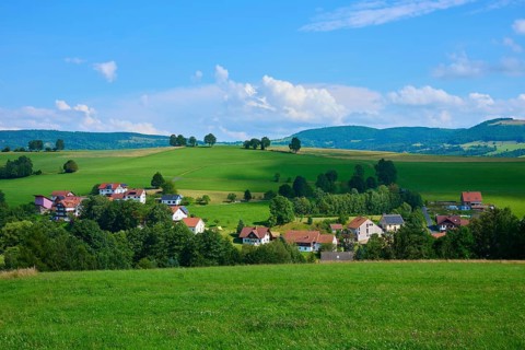 Small village nestled in a hilly landscape with green meadows and trees under a blue sky,