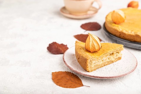 Autumn onion pie decorated with leaves and cup of coffee on gray concrete background. Side view,