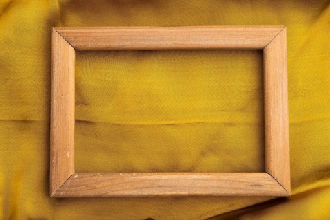 Wooden frame on smooth yellow silk tissue. Top view, flat lay, natural textile background and