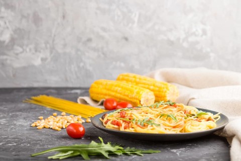 Corn noodles with tomato sauce and arugula on a black concrete background and linen textile. Side
