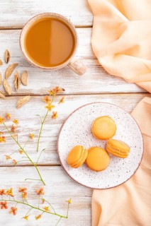 Orange macarons or macaroons cakes with cup of apricot juice on a white wooden background and