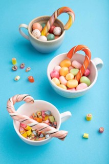 Heap of multicolored caramel candies in cups on blue pastel background. close up, side view