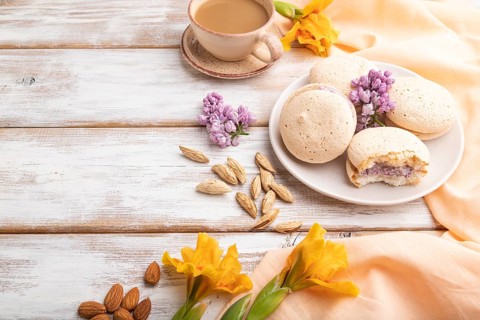 Meringues cakes with cup of coffee on a white wooden background and orange linen textile. Side