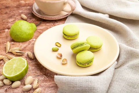 Green macarons or macaroons cakes with cup of coffee on a brown concrete background and linen