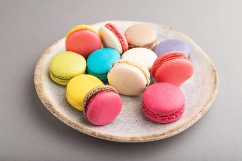 Multicolored macaroons on ceramic plate on gray pastel background. side view, close up, still life.