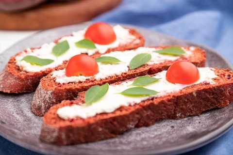 Red beet bread sandwiches with cream cheese and tomatoes on white concrete background and blue