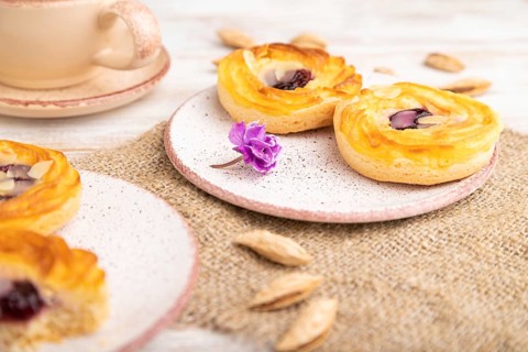 Small cheesecakes with jam and almonds with cup of coffee on a white wooden background and linen