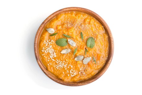 Sweet potato or batata cream soup with sesame seeds in a wooden bowl isolated on a white background