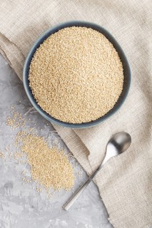 Blue ceramic bowl with raw white quinoa seeds on a gray concrete background and linen textile. Top