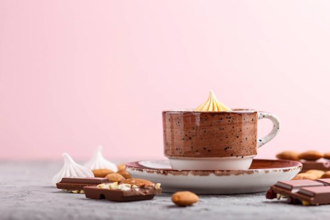 Cup of hot chocolate and pieces of milk chocolate with almonds on a gray and pink background. side