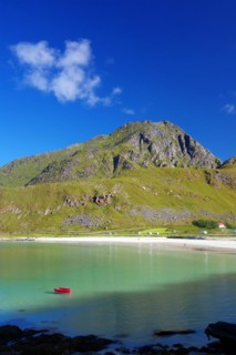 Fine, crystal-clear sandy beach with turquoise-green water and a red boat, high mountains, Haukland