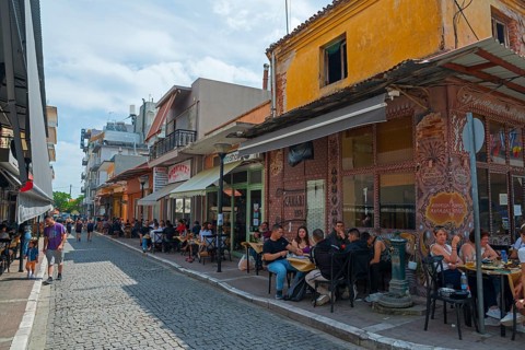 People enjoying food and drinks in outdoor seating along a lively street, Alexandroupoli,