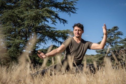 A middle-aged Caucasian man practices Kung Fu on a hill, performing stretching, balancing, and