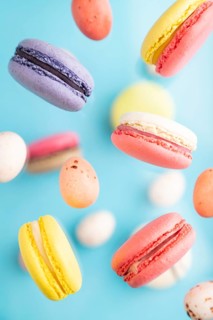 Multicolored flying macaroons and chocolate eggs frozen in the air on blurred blue background. top