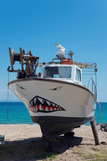 A small fishing boat with a painted shark face on the beach in front of a clear sky, shipyard,