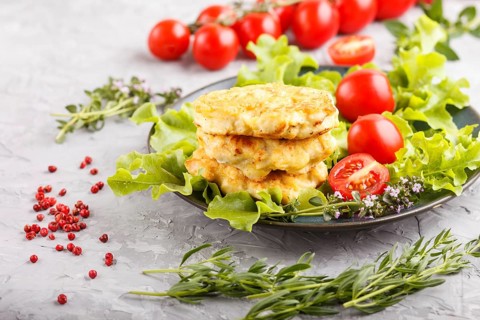 Minced chicken cutlets with lettuce, tomatoes and herbs on a gray concrete background. side view,