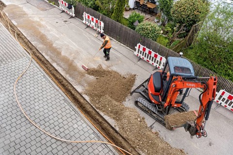 Construction workers lay fibre optic cable in trench under asphalt, cable trench, excavator,